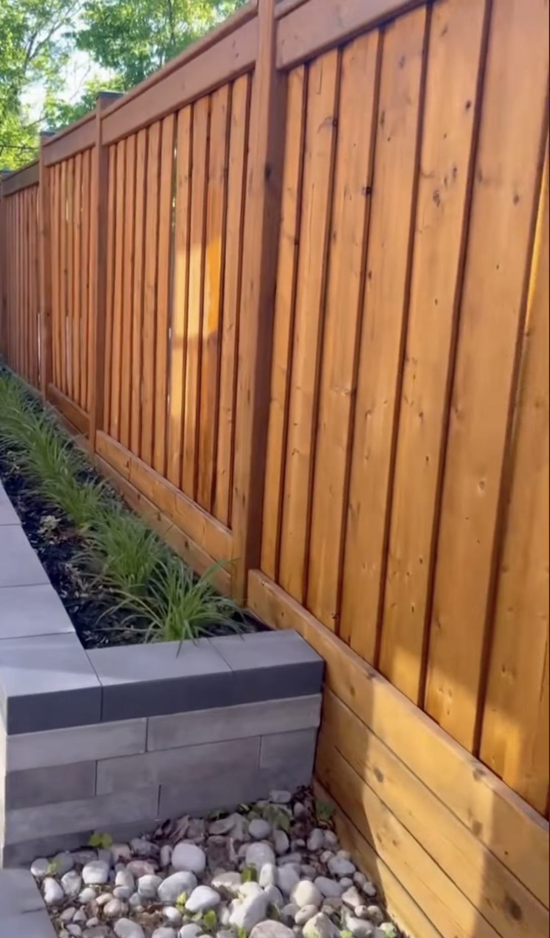 Freshly stained cedar privacy fence running alongside a stone garden bed