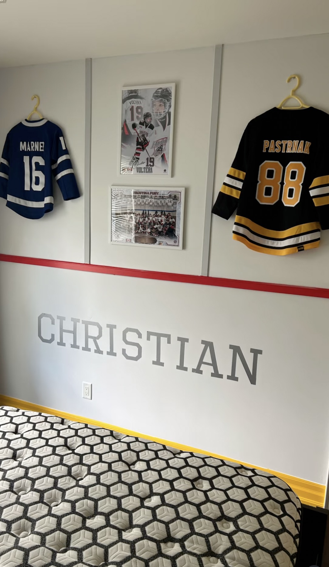 Bedroom wall with a red stripe, a name in large grey letters, and two hockey jerseys mounted above